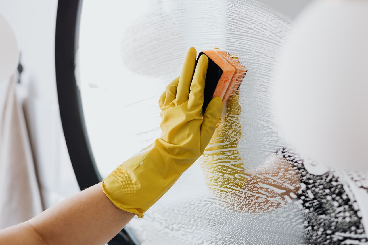 expertise-01 Anonymous person in yellow rubber gloves using simple sponge for cleaning mirror in bathroom